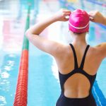 Swimmer adjusting cap near an indoor pool.
