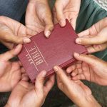 Rev. Hall’s Unique Approach to Bridging Political Gaps at Church Multiple hands holding a red Bible together.