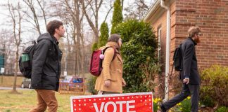 People walking into building beside "Vote" sign.