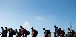 Line of people walking with backpacks outdoors.