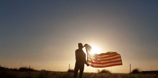 Silhouette holding USA flag against sunset sky
