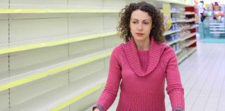 Woman with cart in store with empty shelves.