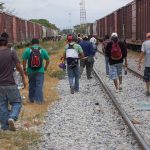 People walking along train tracks carrying backpacks