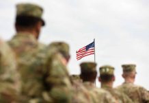 Soldiers standing with American flag in background sky