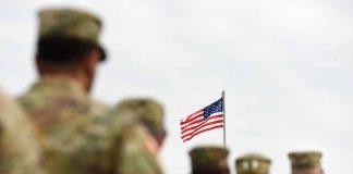 Soldiers standing with American flag in background sky