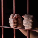 Hands gripping rusty prison bars in darkness