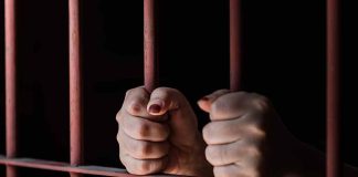 Hands gripping rusty prison bars in darkness