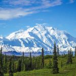 Snow-covered mountain under blue sky with green foreground.