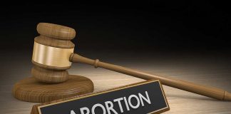 Gavel and sign reading "Abortion" on a wooden surface.