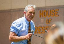 Man speaking with microphone outside building with lettering