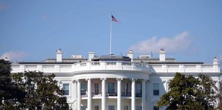 White House with American flag flying, daytime.