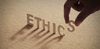 Hand placing the letter S in the word ETHICS.