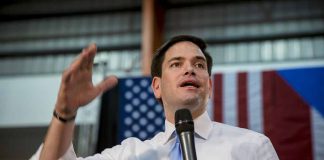 Man speaking with microphone indoors near flags