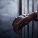 Longstanding Prison Faces New Legal Accusations After Inmate Tragedy Hands gripping prison cell bars.