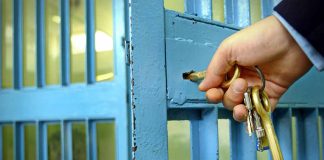 Hand unlocking blue prison cell with keys