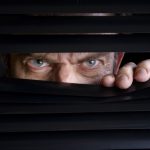 Man peeking through half-open black blinds.