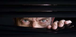 Man peeking through half-open black blinds.