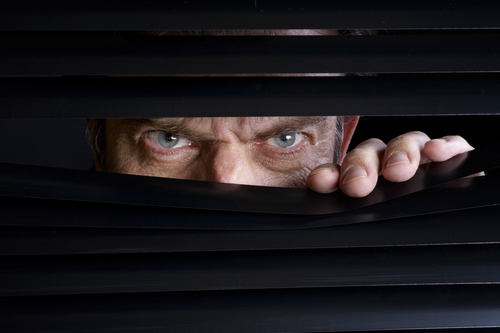 Man peeking through half-open black blinds.