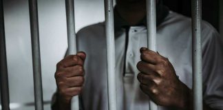 Person holding jail cell bars tightly