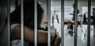 Person sitting behind bars with arms wrapped around knees