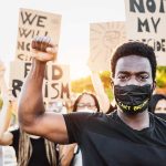 Protester raises fist wears mask signs in background
