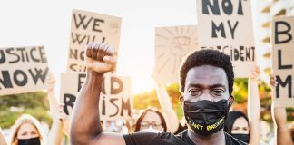 Protester raises fist wears mask signs in background