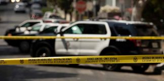Police tape blocking street with patrol cars