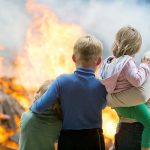 Three children and adult watching large fire outdoors