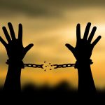 Hands breaking free from chains at sunset