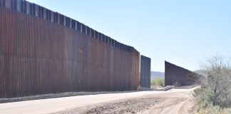 Dirt road beside tall metal border wall