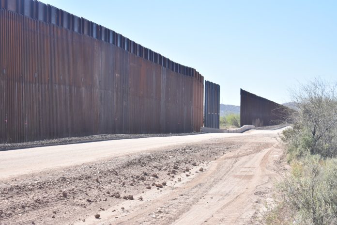 shutterstock_1958049433.jpg featured image Dirt road beside tall metal border wall