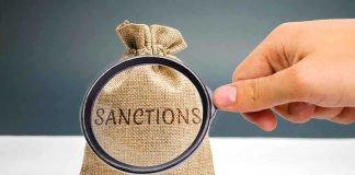 Hand holding magnifying glass over sack labeled Sanctions