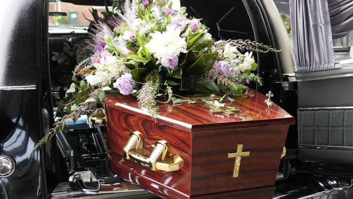 1785607928 Coffin with flower arrangement in a hearse