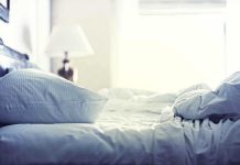 A cozy unmade bed with soft pillows and bedding in a lit room