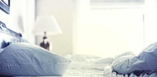 A cozy unmade bed with soft pillows and bedding in a lit room