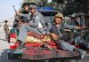 Three armed soldiers sitting on the back of a military vehicle in an urban setting