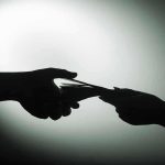 Bribe Scandal Erupts—Top Adviser INDICTED Silhouette of hands exchanging money in dim light.