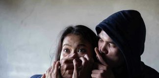 Man holding woman's mouth, gesturing silence.