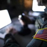 Soldier using laptop with US flag patch visible