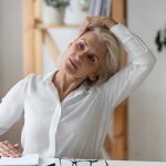 Woman stretching neck at a desk indoors