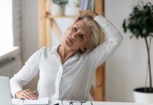 Woman stretching neck at a desk indoors