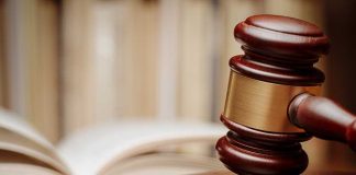 A wooden gavel resting on a sound block with law books in the background