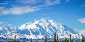 Snow-covered mountain under blue sky with green foreground.