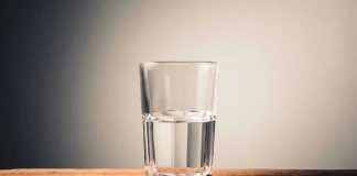 Glass of water half full on table.