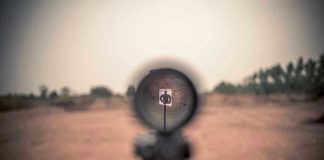 Rifle scope aimed at a distant target outdoors.