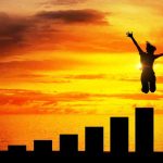 Silhouette jumping above bar chart at sunset.