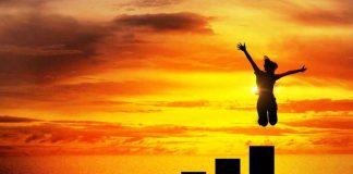 Silhouette jumping above bar chart at sunset.