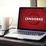 Laptop screen displaying CENSORED beside coffee and phone
