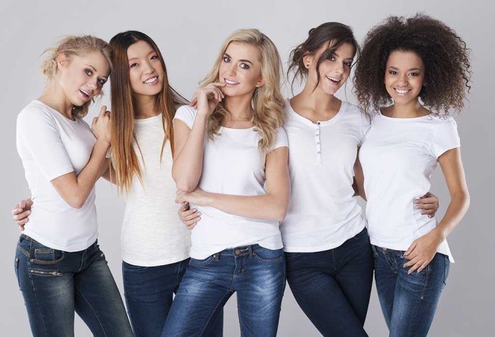 Five women in white t-shirts and jeans smiling together