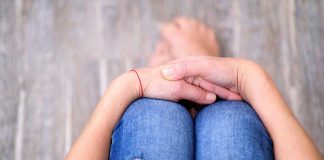 Person sitting with folded hands on knees.